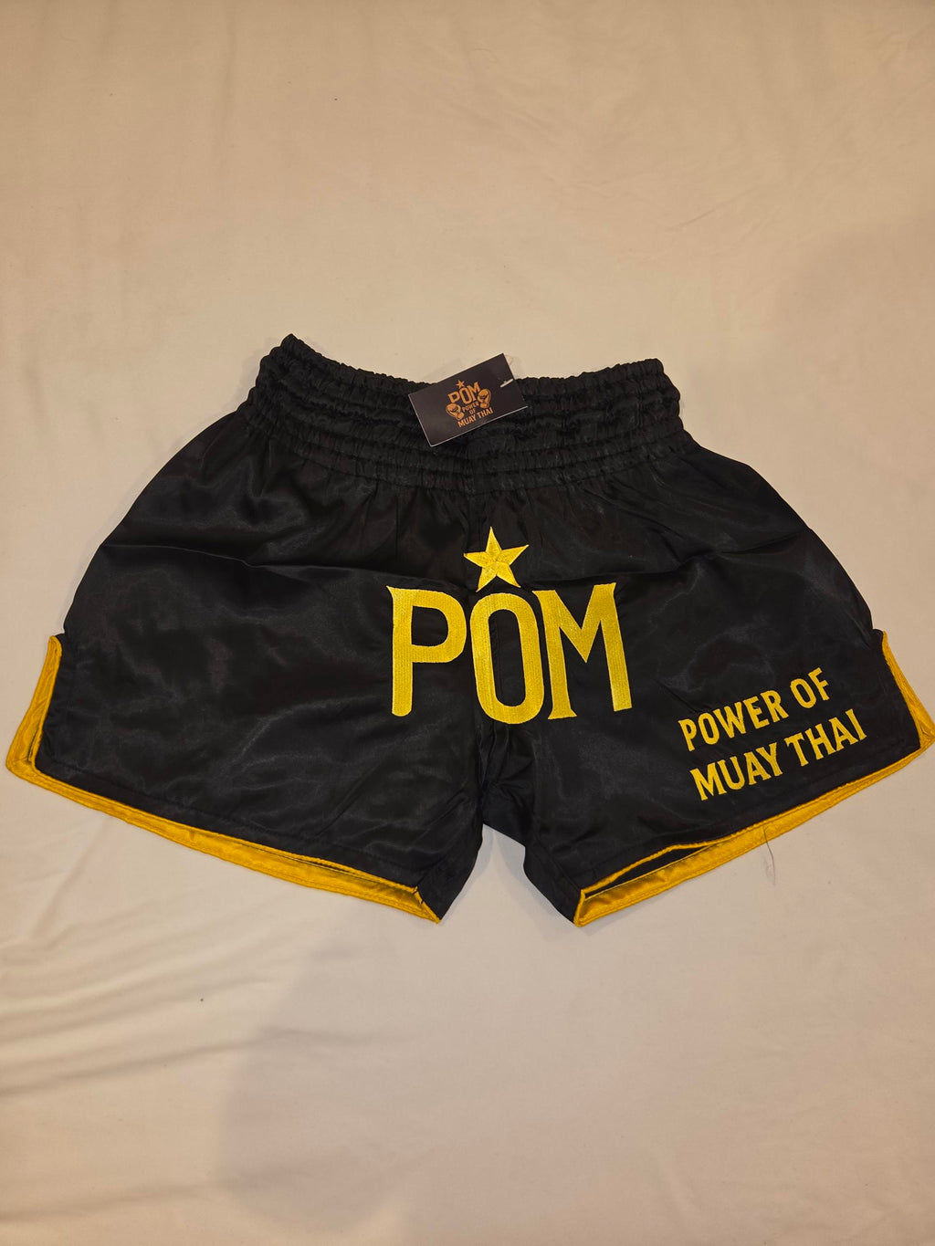 P.O.M Muay Thai Shorts Star Edition – schwarz mit großem gold gesticktem POM-Logo und Stern, Goldsaum