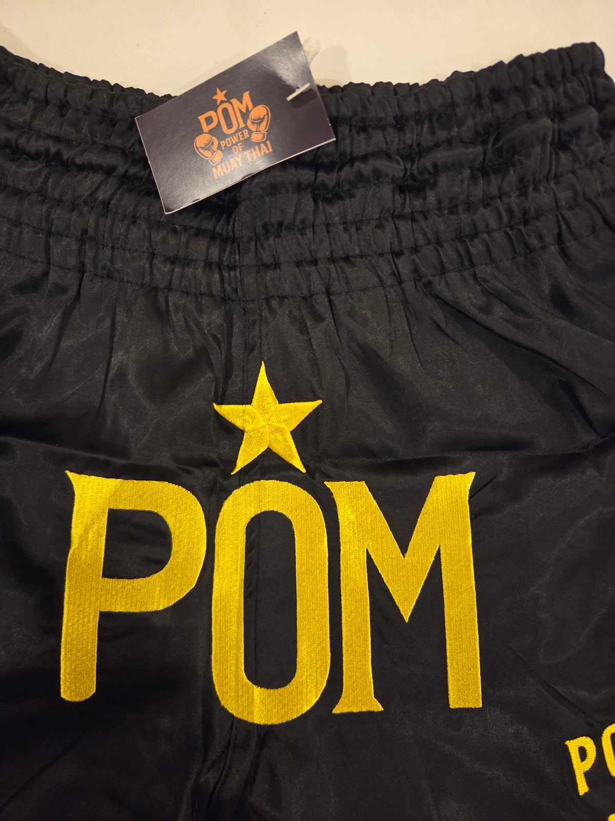 Nahaufnahme der Goldstickerei: POM-Logo mit Stern auf schwarzem Satin
